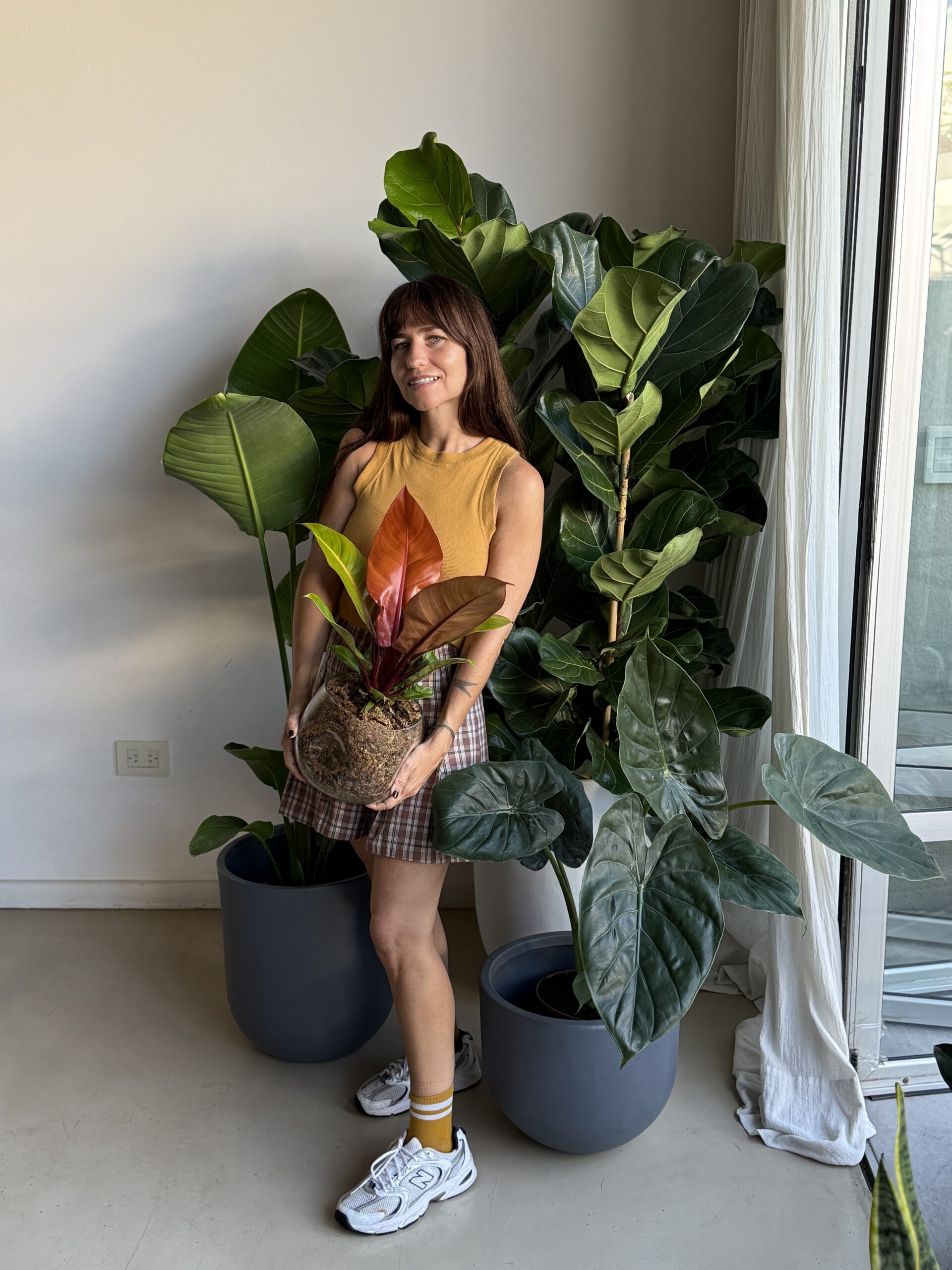 Mujer rodeada de plantas en macetas de distintas alturas y tonos en living, ejemplo de cómo combinar macetas